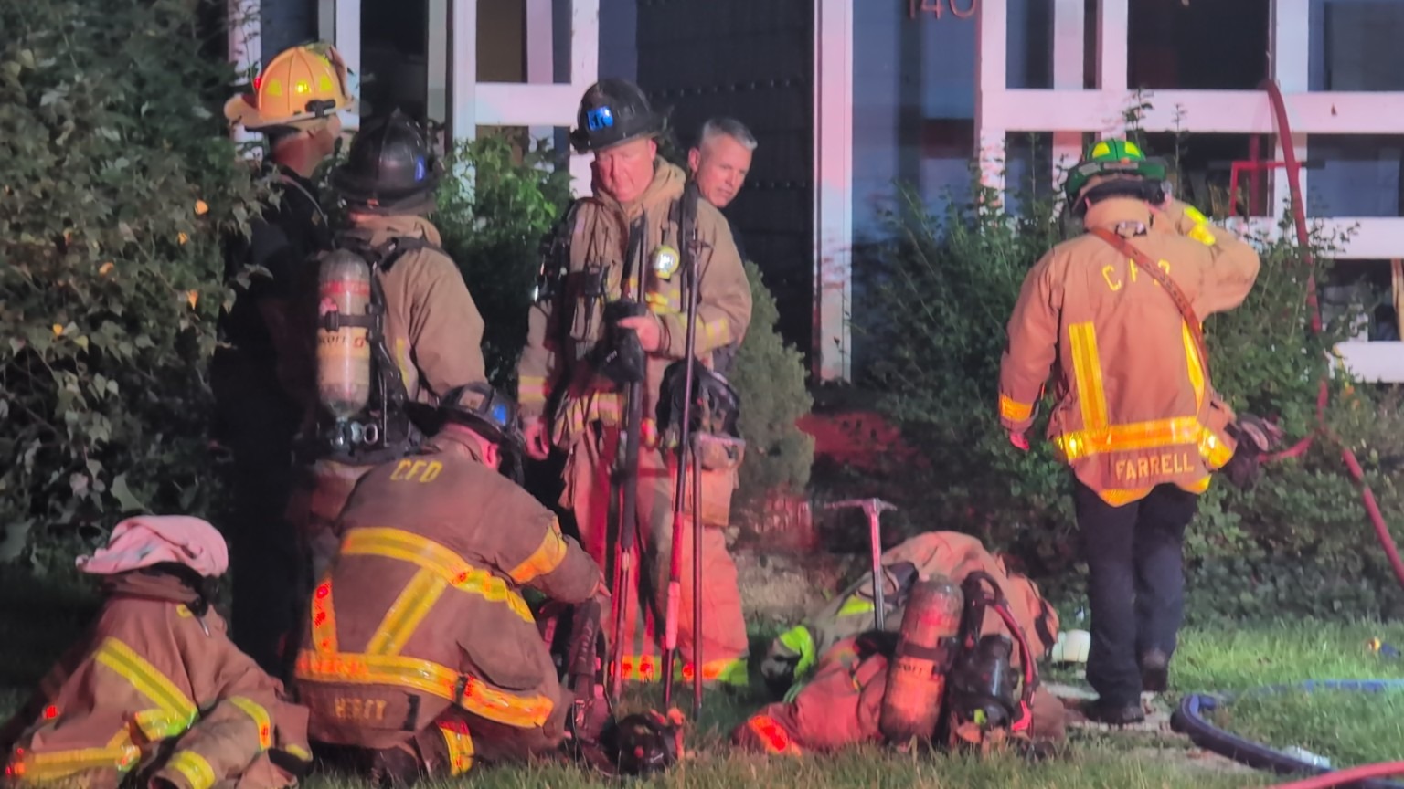 Firefighters gathered beside a building at night.